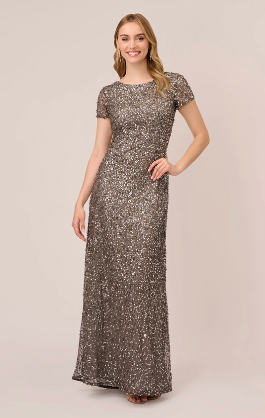 A model wearing a sleeveless, sequin evening dress with a scoop back and a flowing skirt.