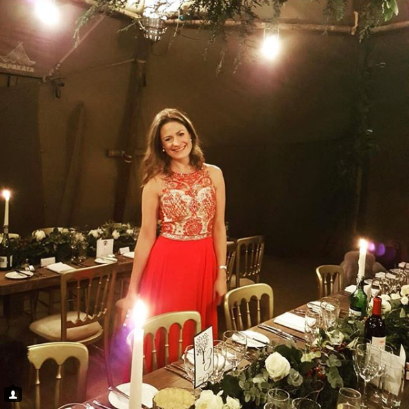 Woman in a red dress standing in a dimly lit room with a decorated table and floral arrangements.